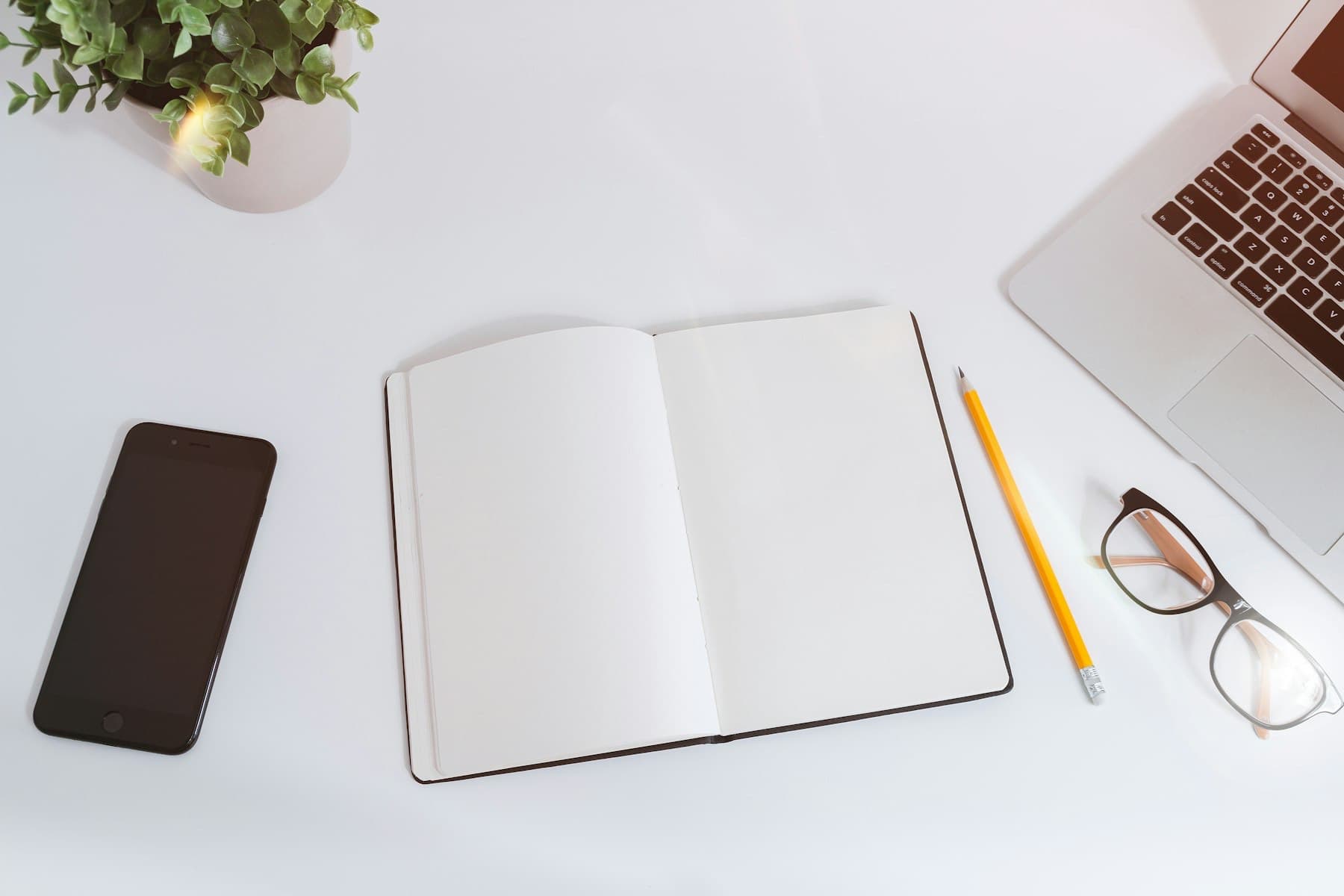 Open notebook, pen and glasses on a white desk